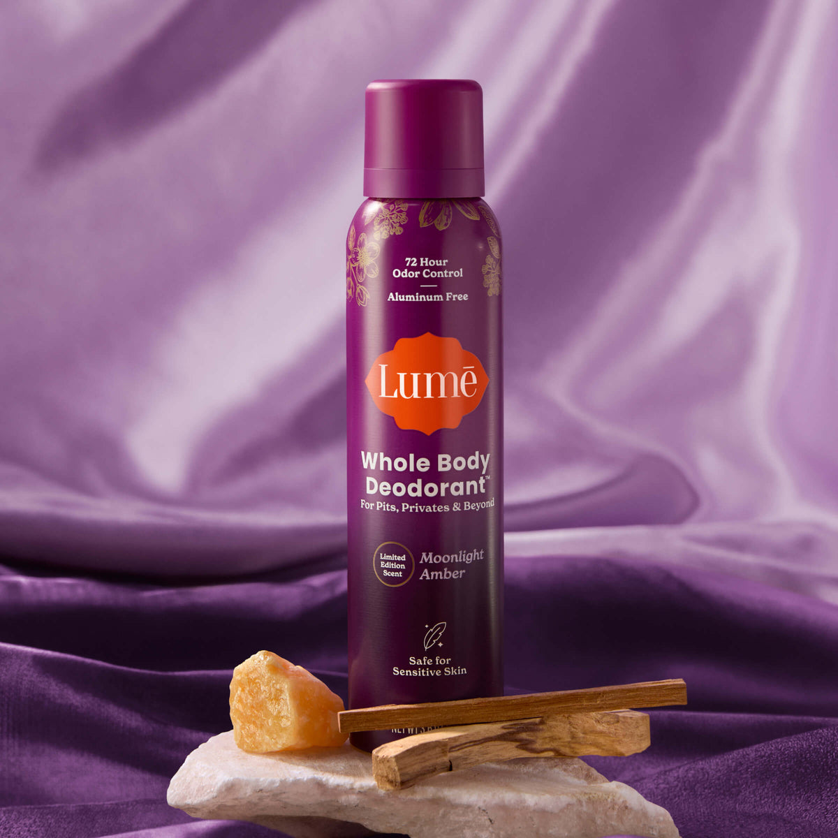 Spray deodorant on top of a rock, next to crystals and luxe fabric.