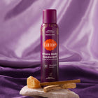 Spray deodorant on top of a rock, next to crystals and luxe fabric.