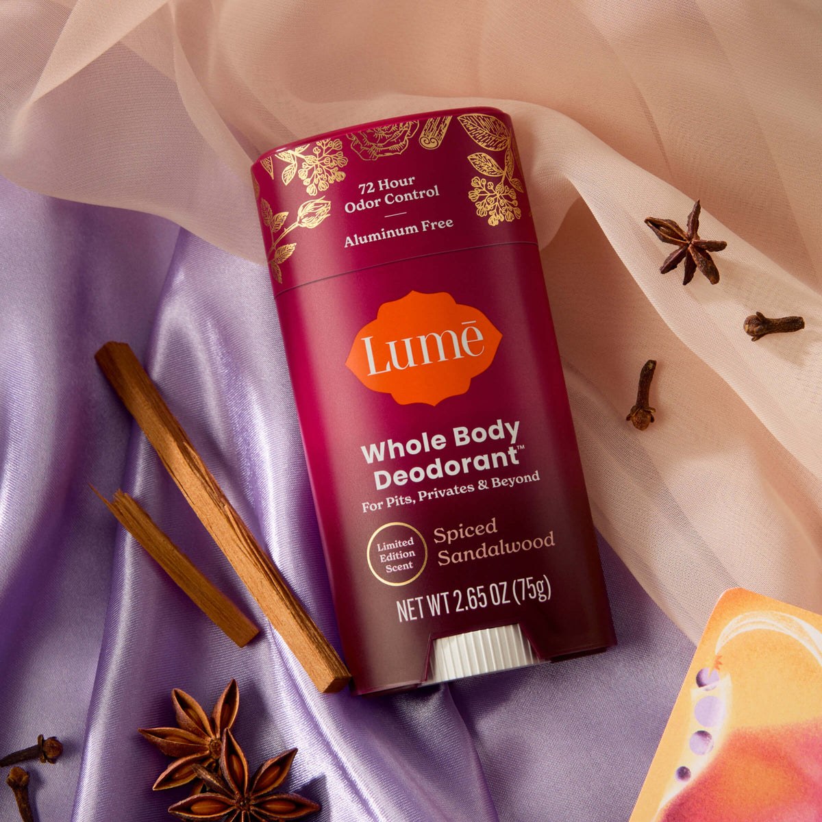 Lume Spiced Sandalwood deodorant on top of fabric and surrounded cinnamon sticks, cloves, and star anise.